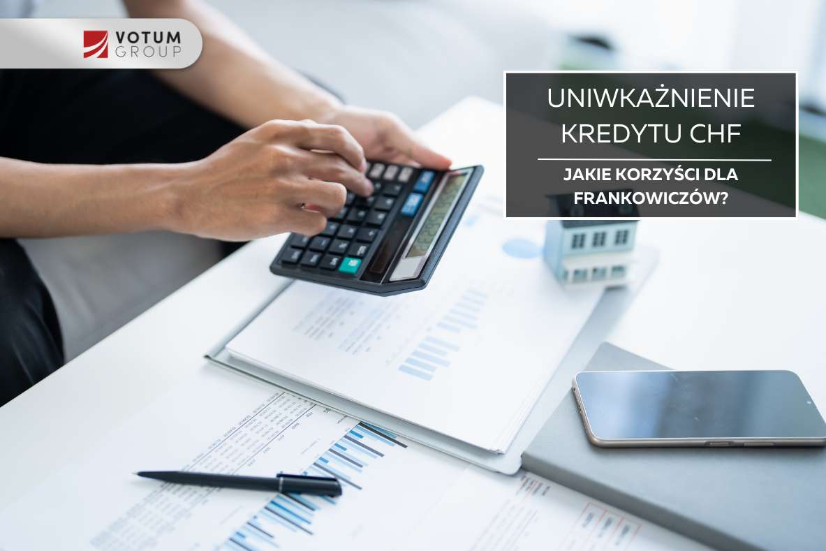 Osoba trzymająca kalkulator nad biurkiem z dokumentami dot. kredytu frankowego