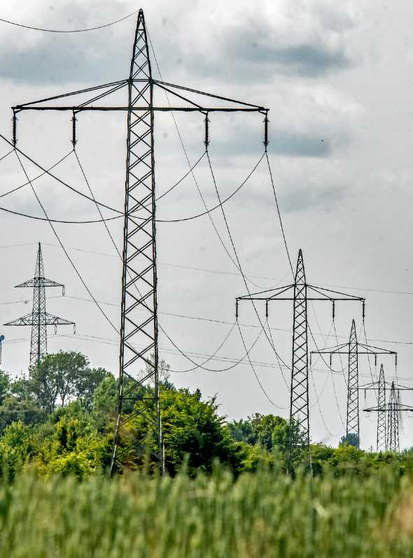 sluzebnosc-przesylu-odszkodowanie-pomoc Kilka wysokich stalowych słupów linii energetycznych rozciągających się nad polem obsadzonym zielonymi roślinami, pod pochmurnym niebem.