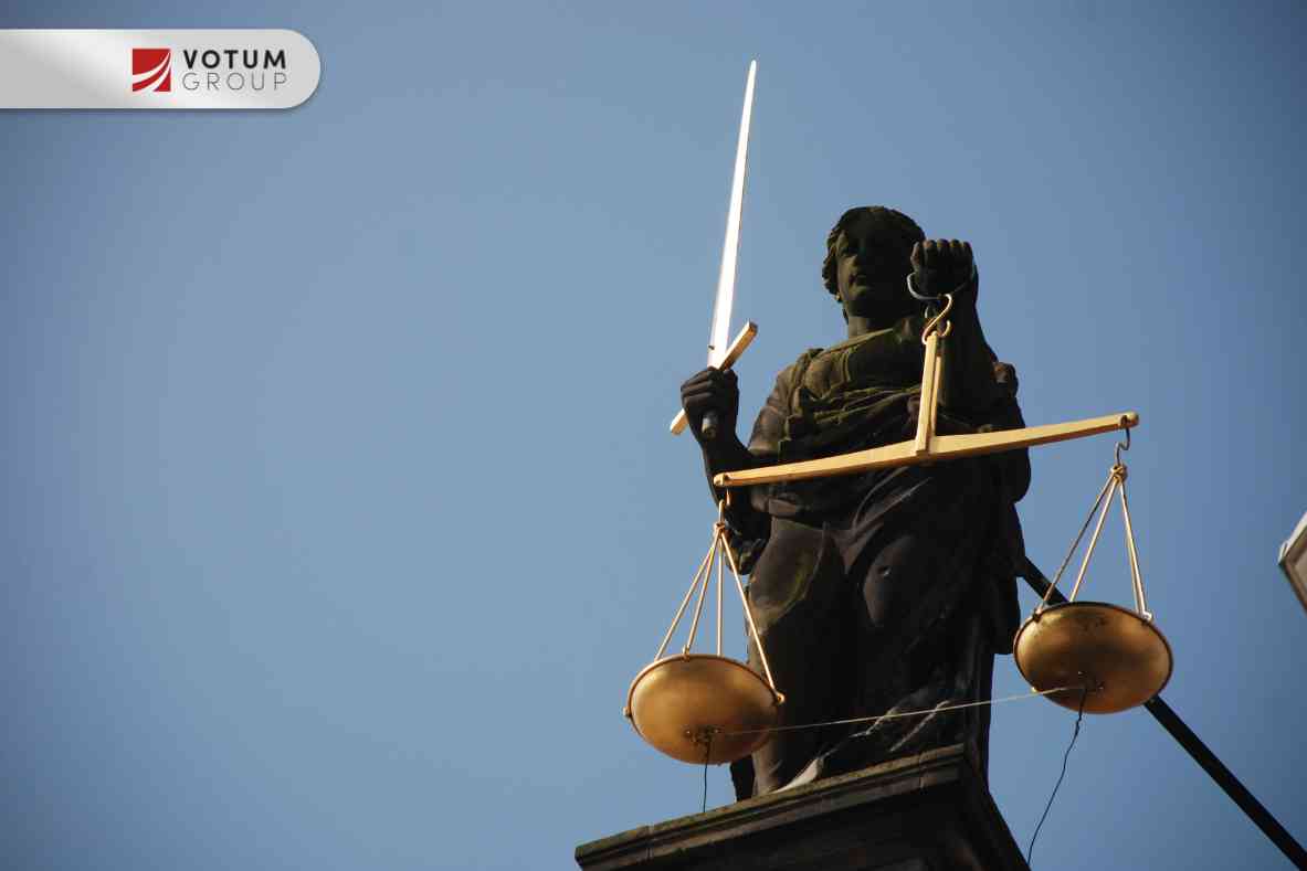 Widok z dołu na ciemny posąg Temidy trzymającej wzniesiony, lśniący miecz oraz wagę szali na tle czystego, błękitnego nieba.